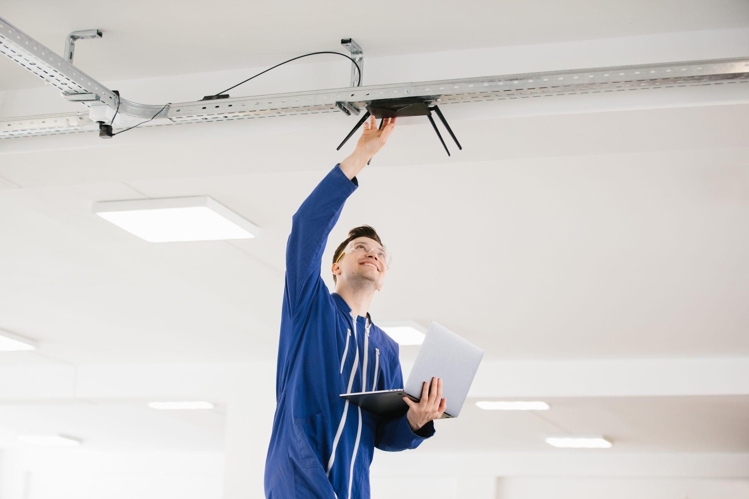 Technician installing wireless router on ceiling using laptop